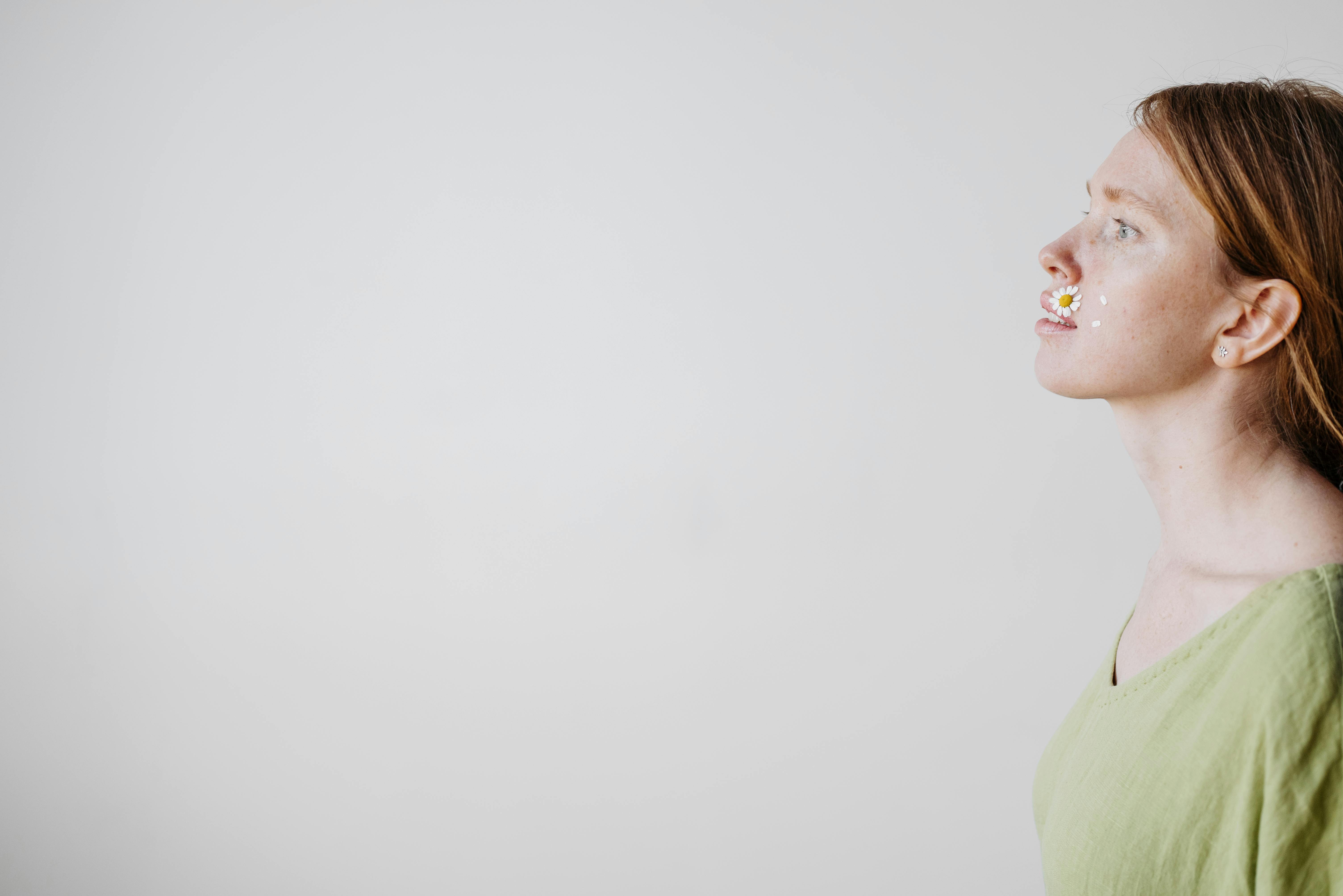 Artistic profile portrait of a redhead woman with daisies on her face, indoors.