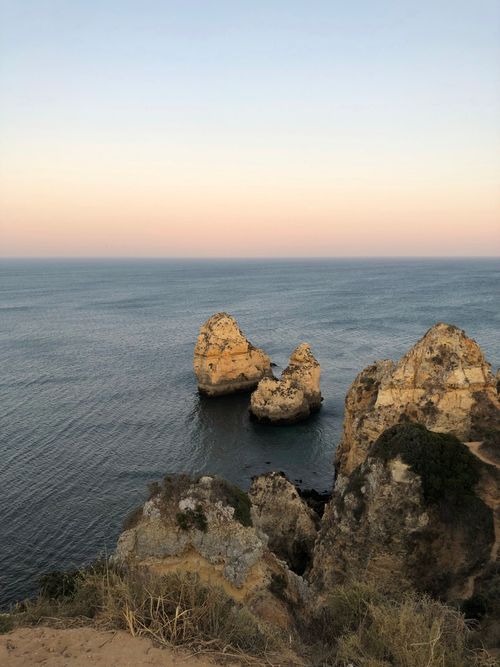 Free A tranquil coastal scene featuring prominent rock formations and a calm ocean at sunset. Stock Photo