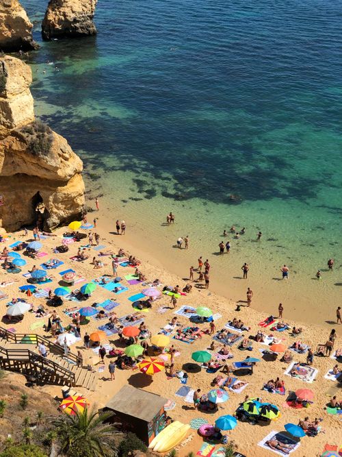Free Colorful umbrellas dot a lively beach with people enjoying the clear blue sea. Stock Photo