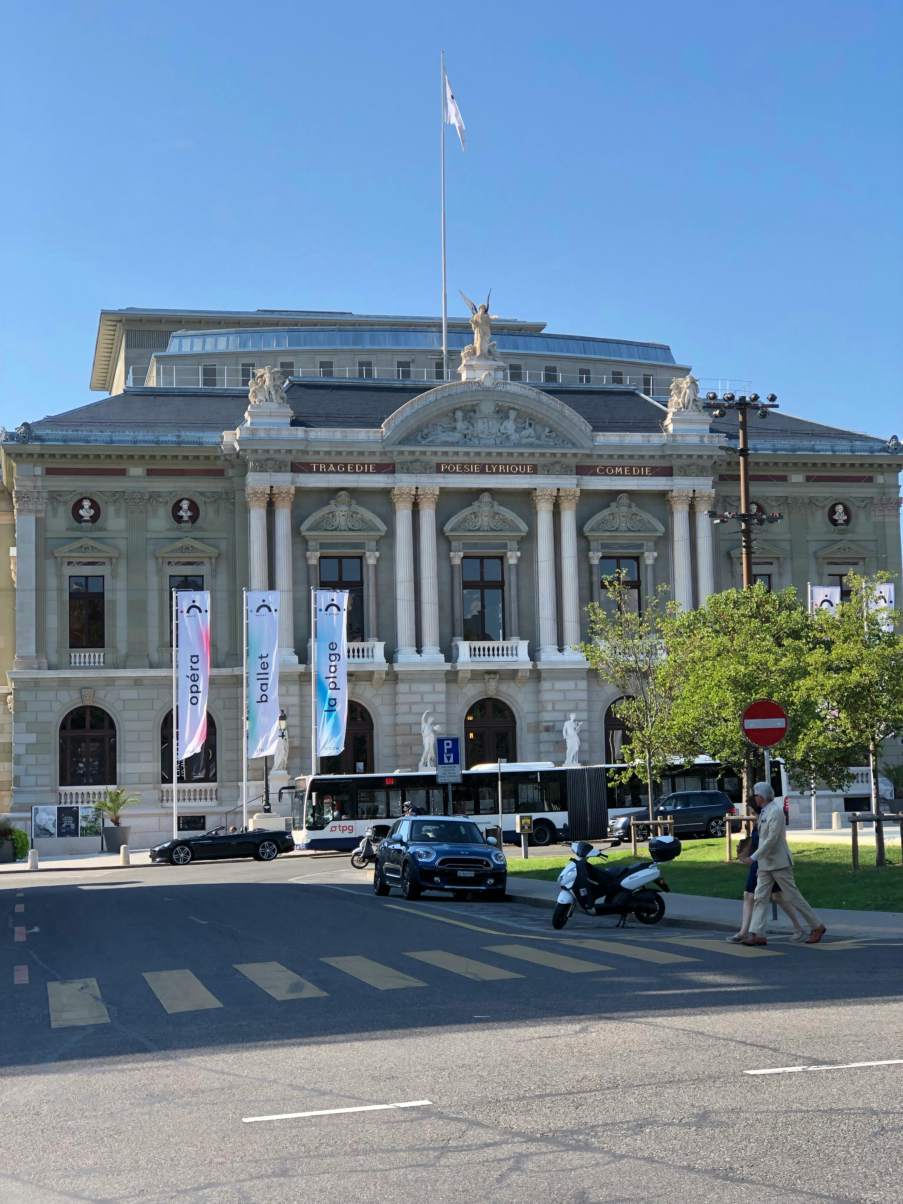 Free Elegant facade of Grand Theatre de Geneve with pedestrians and vehicles in foreground. Stock Photo