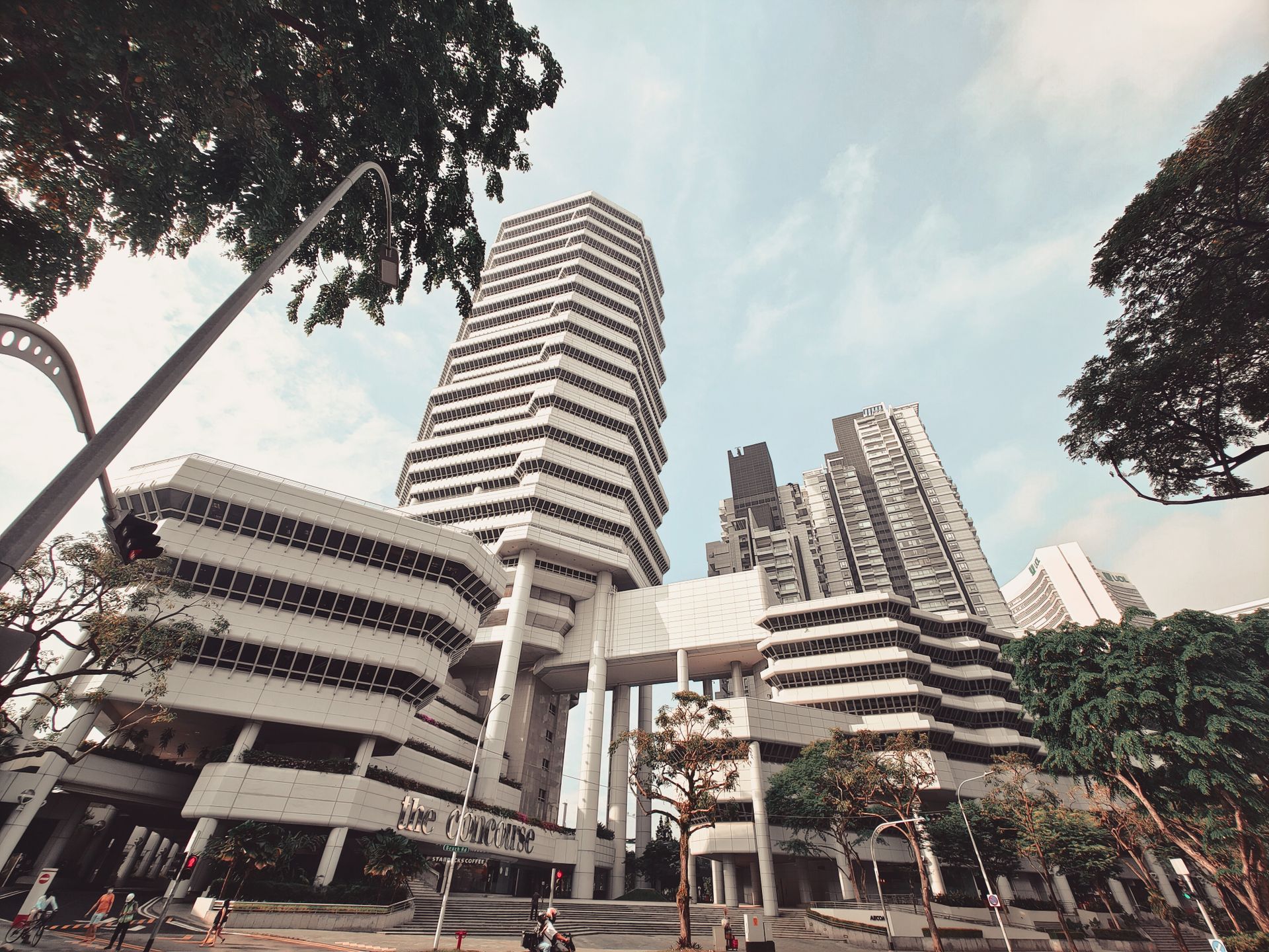 Dramatic low angle view of The Concourse building in Singapore against a blue sky, showcasing modern architecture.