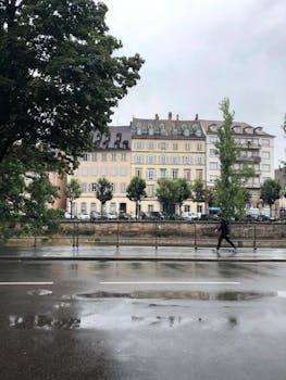 A person walks in the rain along a city street lined with historic European buildings.