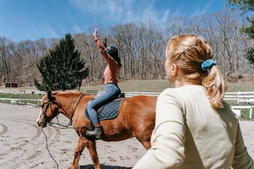 Free Woman learning horseback riding with an instructor in a sunny outdoor setting. Stock Photo