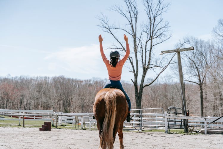 Girl Sitting On A Horse With Her Arms Raised