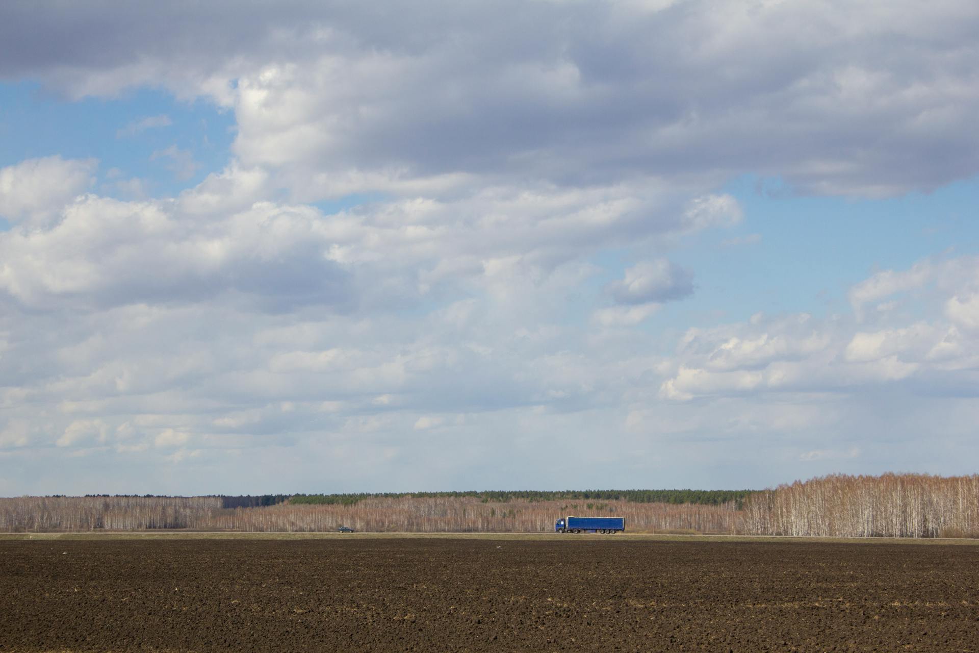 Expansive farmland under a cloudy sky featuring a lone blue truck on a rural road.