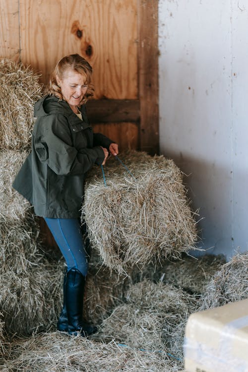 Photo of a Woman in a Green Jacket Carrying Hay