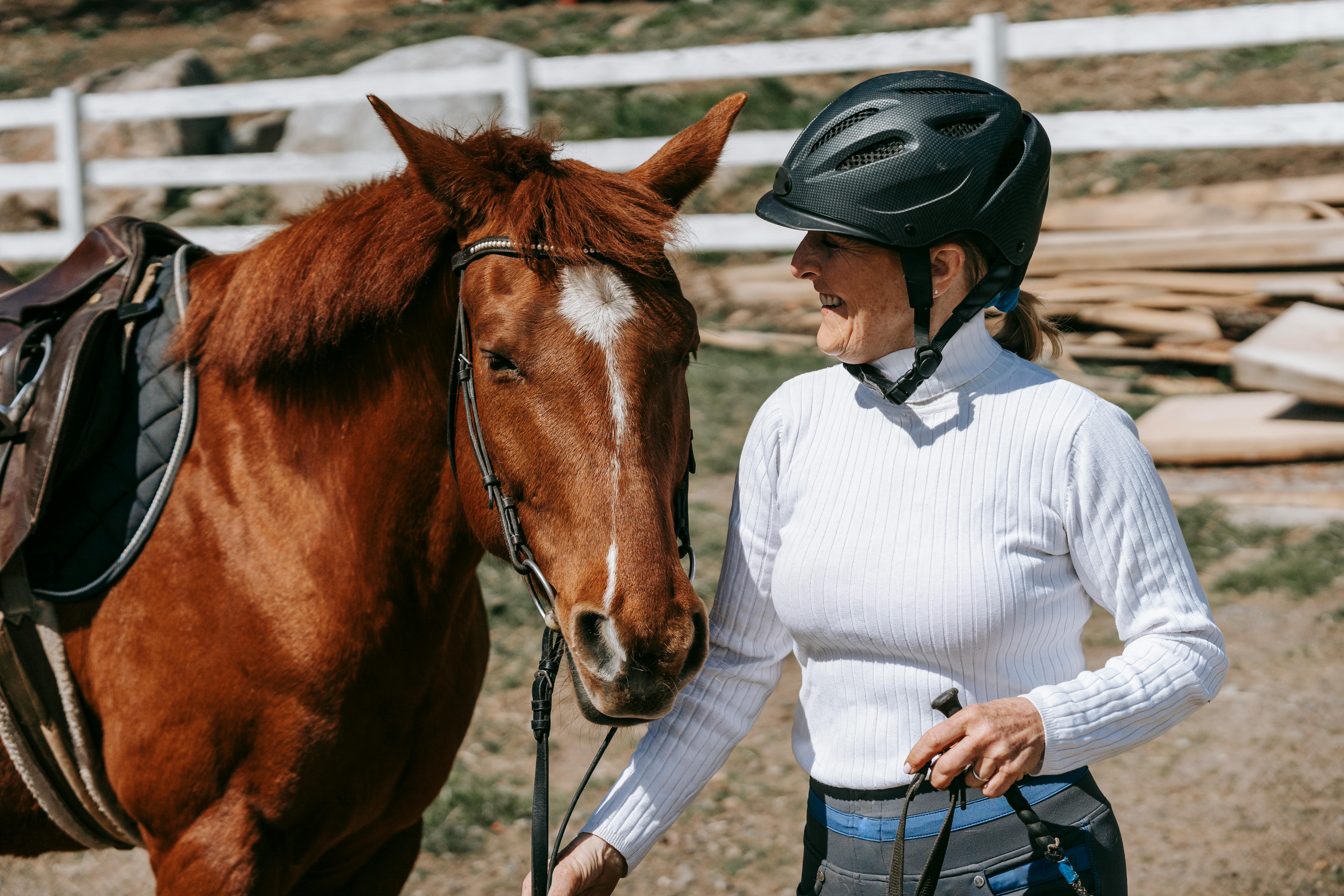 Smiling woman with helmet holding a horse outdoors on a sunny day.