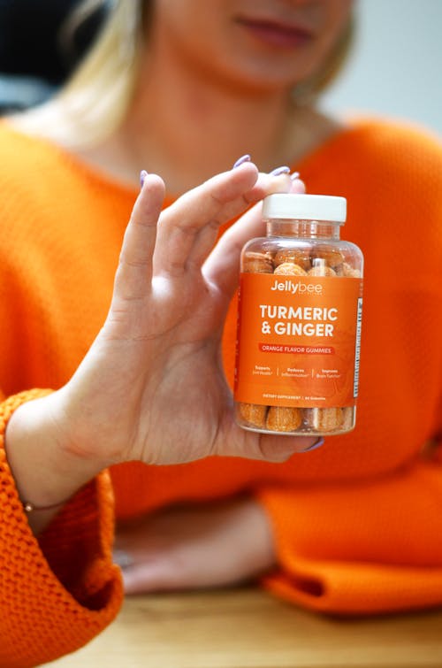Close-Up Shot of a Person Holding a Bottle of Turmeric and Ginger
