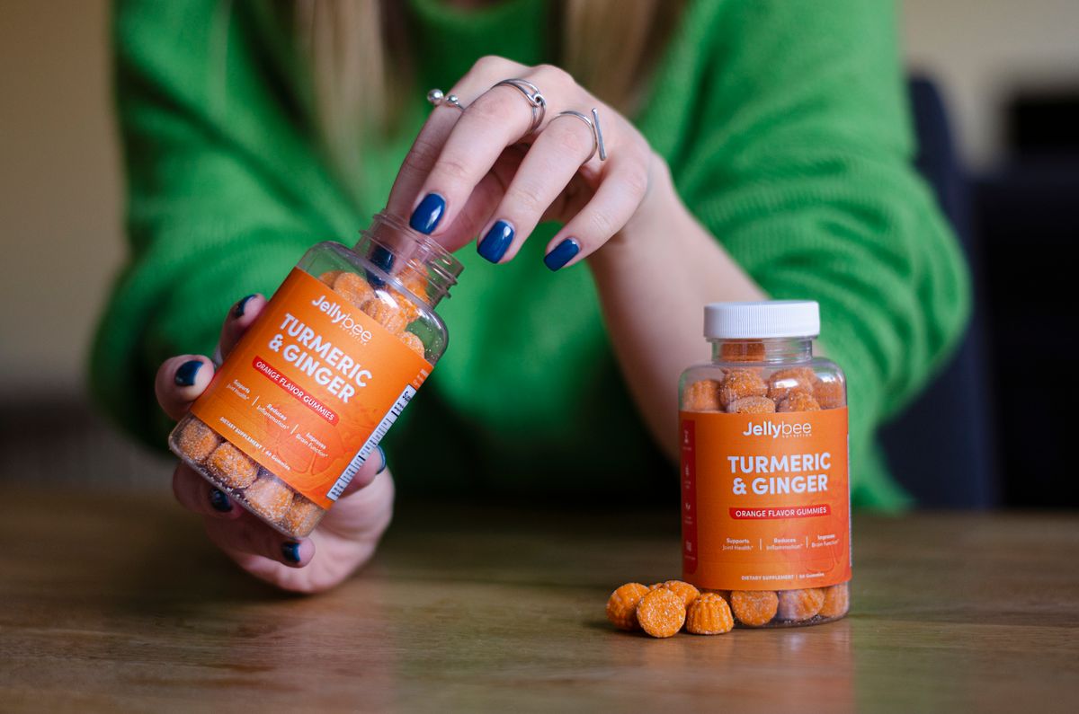 A woman holds and pours Jellybee Turmeric & Ginger gummies, highlighting their vibrant color and health appeal.