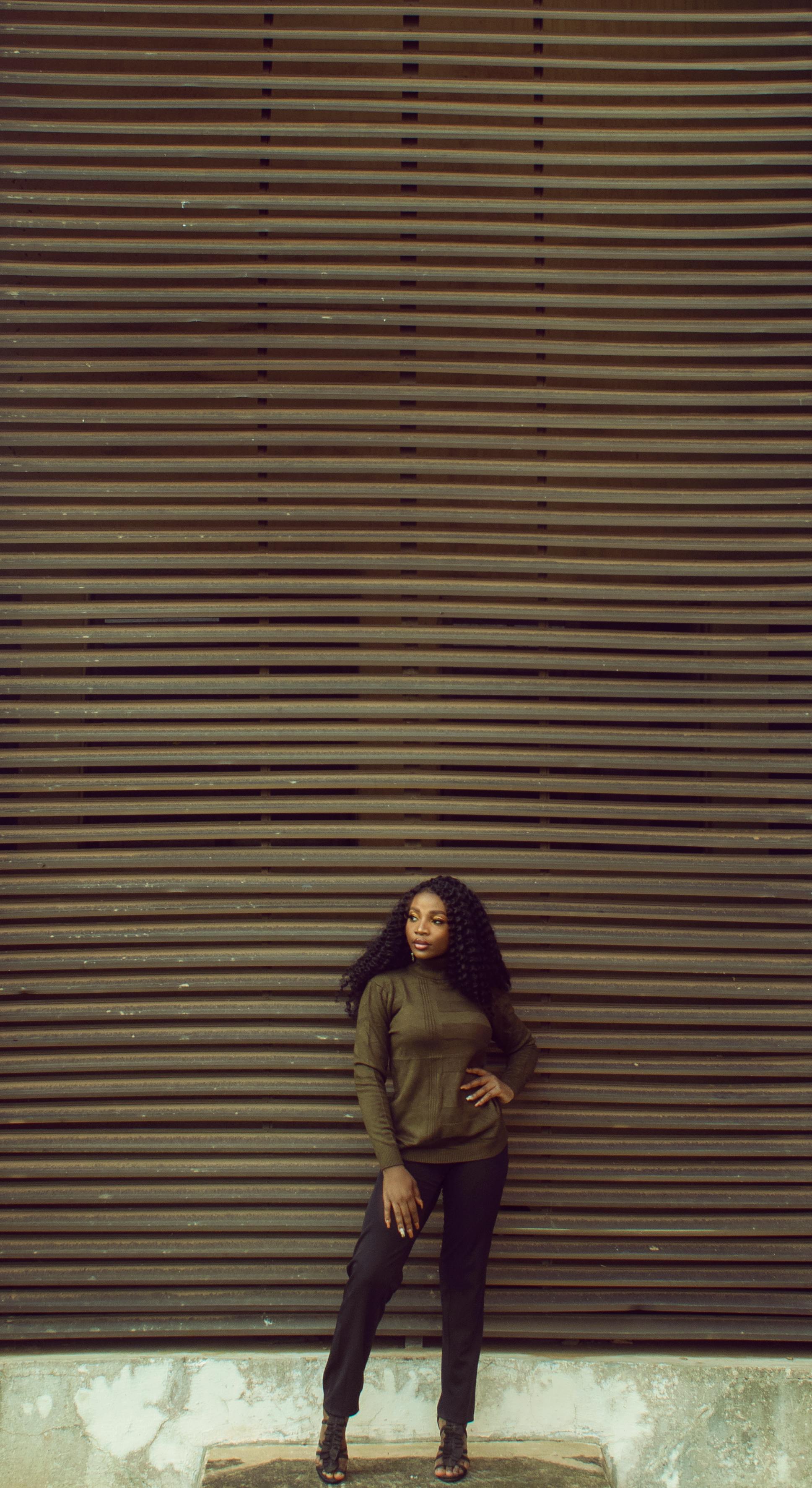 Fashionable woman stands confidently against a large wooden wall, showcasing urban style.