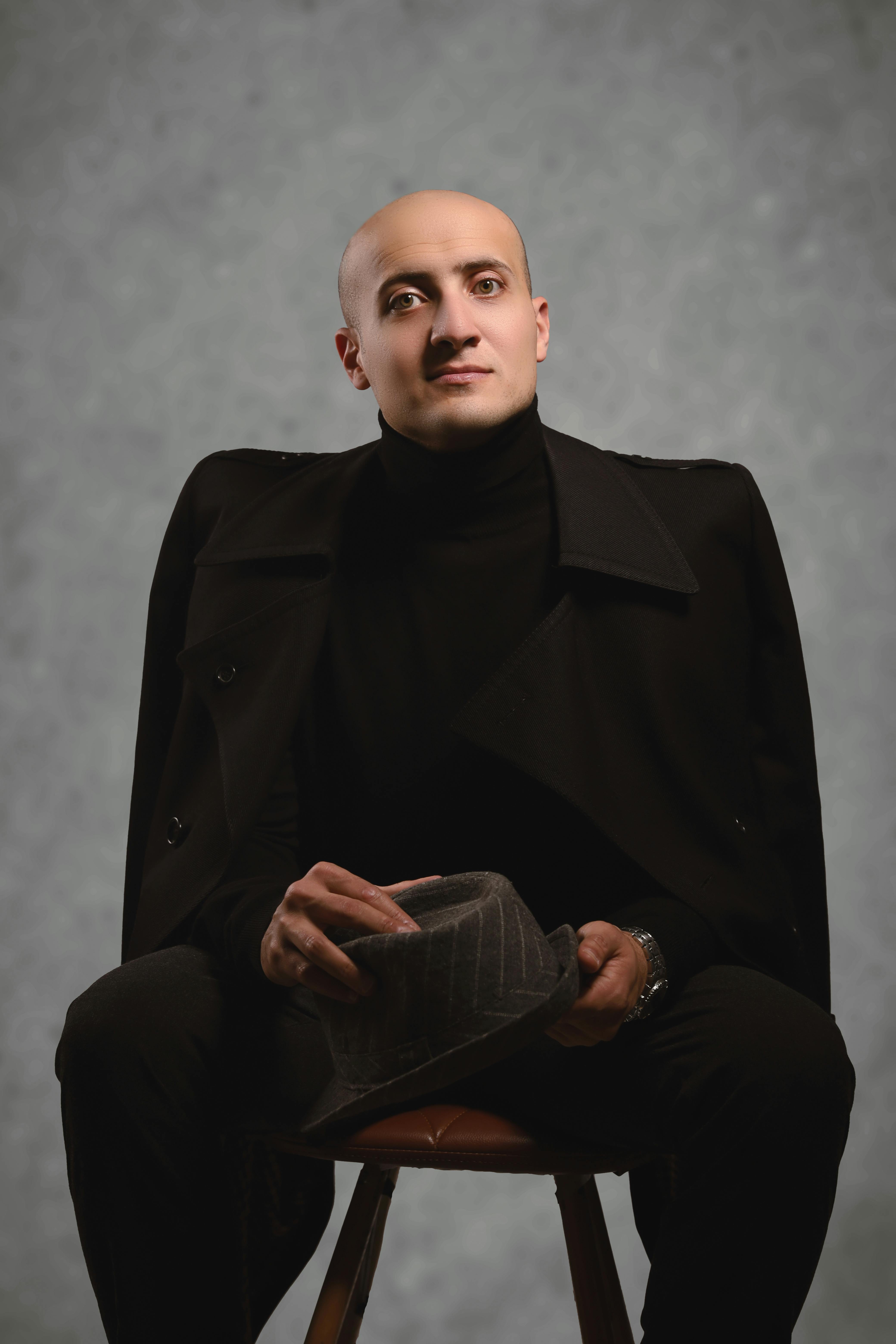 Elegant studio portrait of a man in dark attire holding a hat, exuding confidence and style.