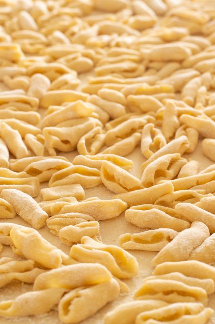 A bowl of small ridged cavatelli pasta shells tossed with tomato sauce and torn basil, showing the curled shape that traps sauce.