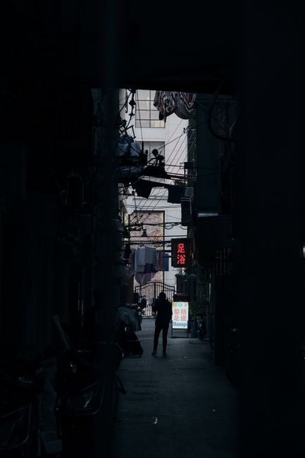 Mysterious city alley at night with a silhouetted person under neon lights.