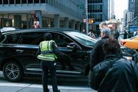 Man in Green and Black Jacket Standing Beside Black Sedan