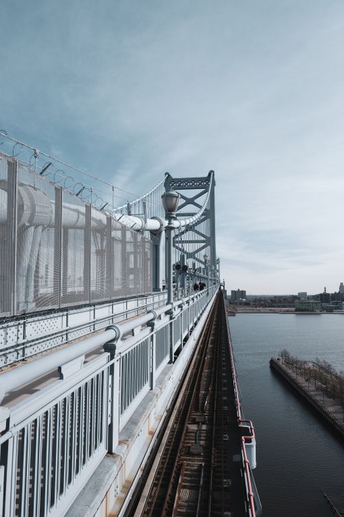 Free Vertical view of the Benjamin Franklin Bridge with a train track and blue sky over the Delaware River. Stock Photo
