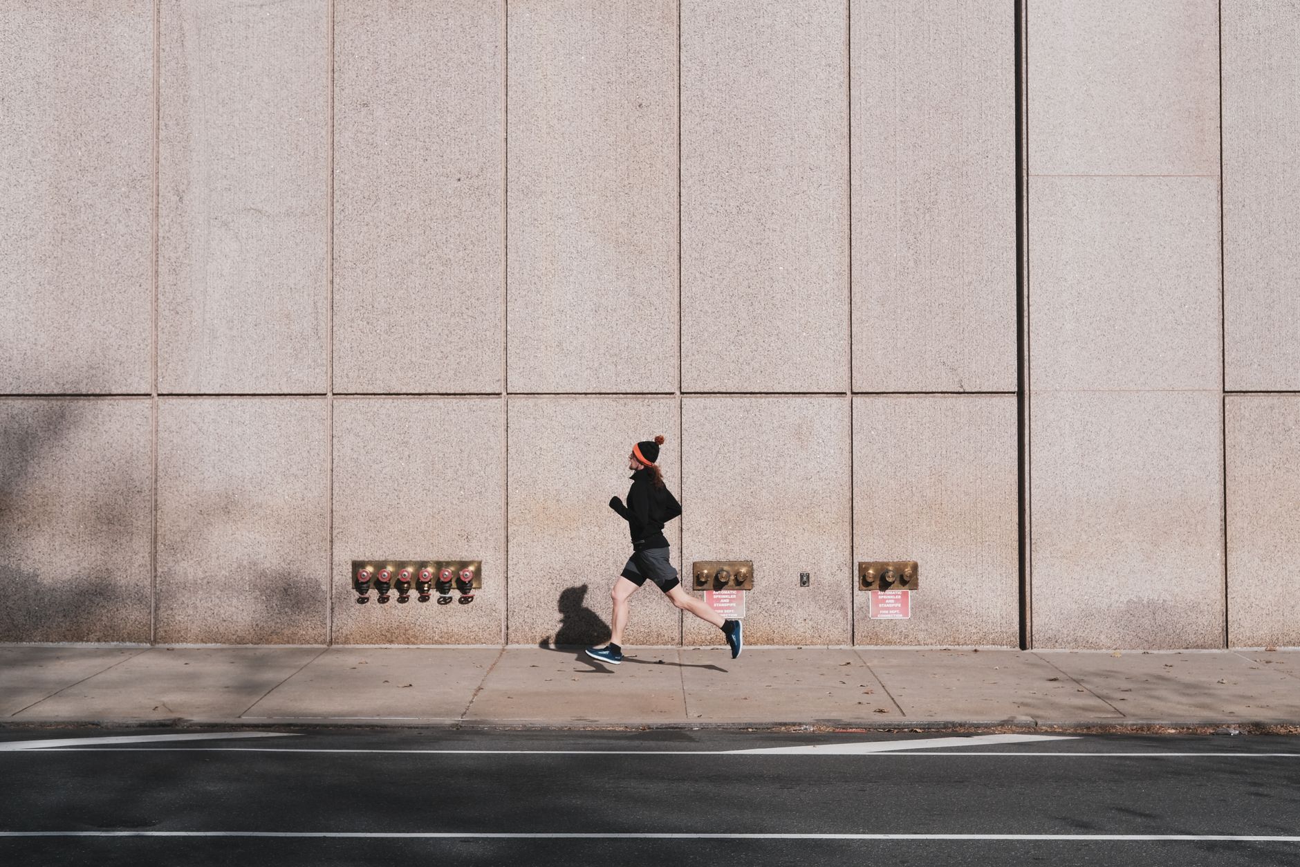 A person jogging along a city sidewalk against a modern urban wall, embracing an active lifestyle.