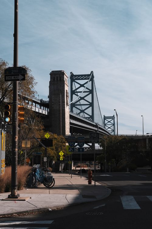 Free View of the Benjamin Franklin Bridge from a Philadelphia street corner, featuring traffic lights and bicycles. Stock Photo