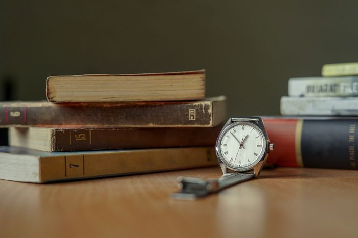 A worn wristwatch resting beside a stack of old books — photo by Yogendra Singh on Pexels