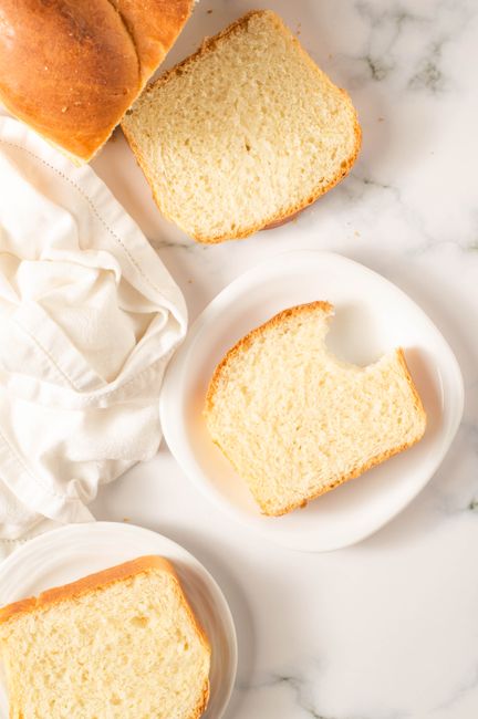 A sliced loaf of sourdough sandwich bread on a wooden board, showing an even, tight crumb with a few slices fanned out next to a butter knife.