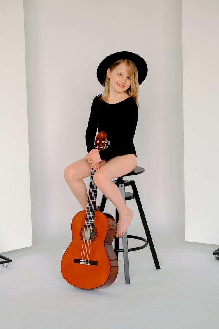 Girl In Black Leotard With Black Hat Sitting On A Stool With A Guitar