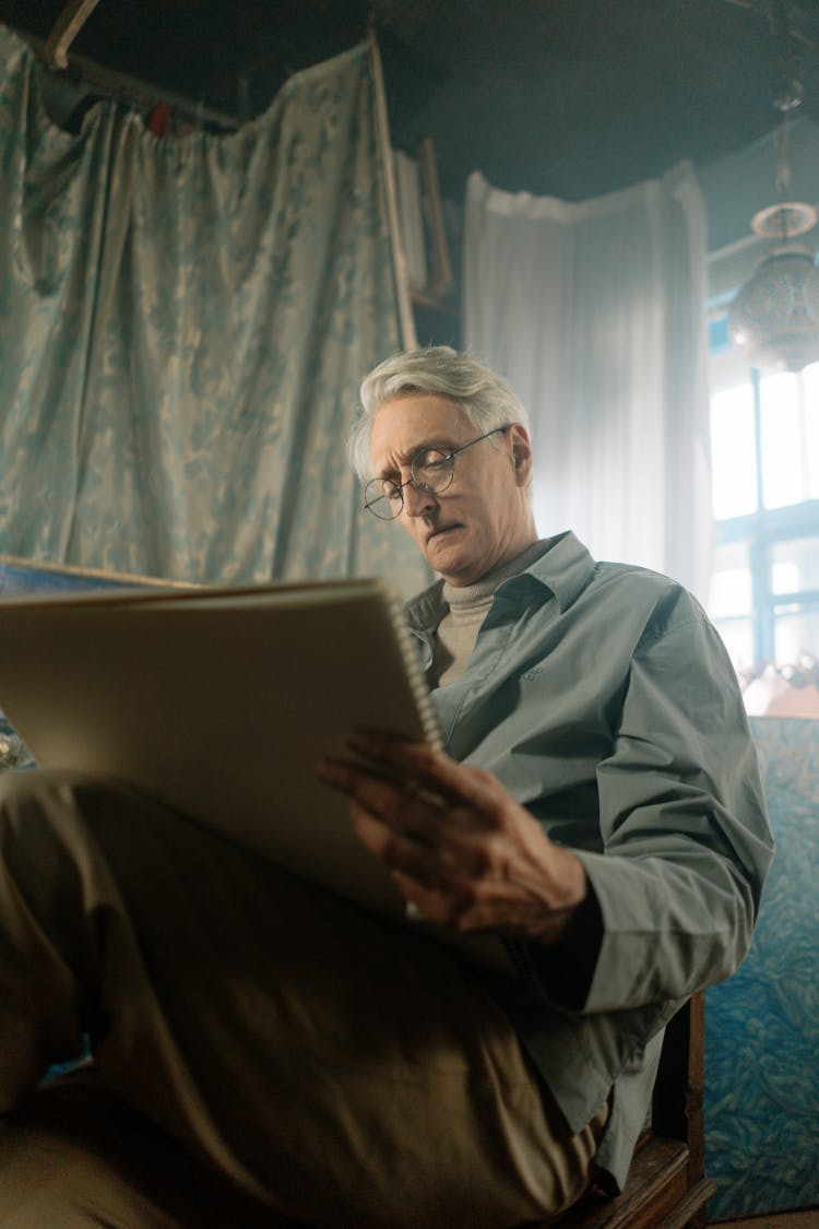 An Elderly Man With Eye Glasses Holding A Sketchbook