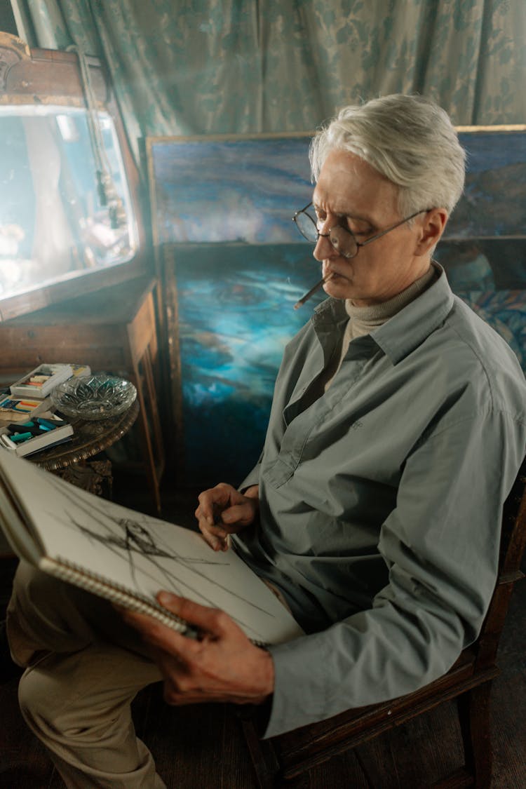 An Elderly Man With Eyeglasses Holding A Sketchbook