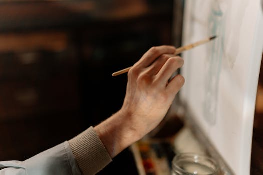 Close-up of an artist's hand painting on a canvas with a brush, capturing creativity.
