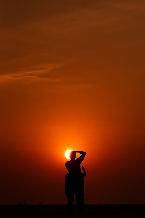 Silhouette of People Facing The Golden Sun Under Red Sky