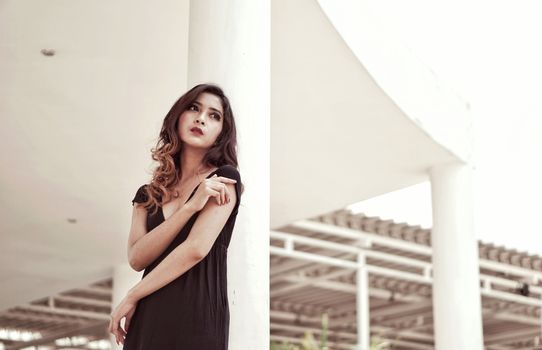 Elegant woman in a black dress posing outdoors against modern architecture.