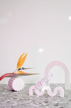A minimalist still life showcasing a cosmetic serum with an exotic flower and modern decor.