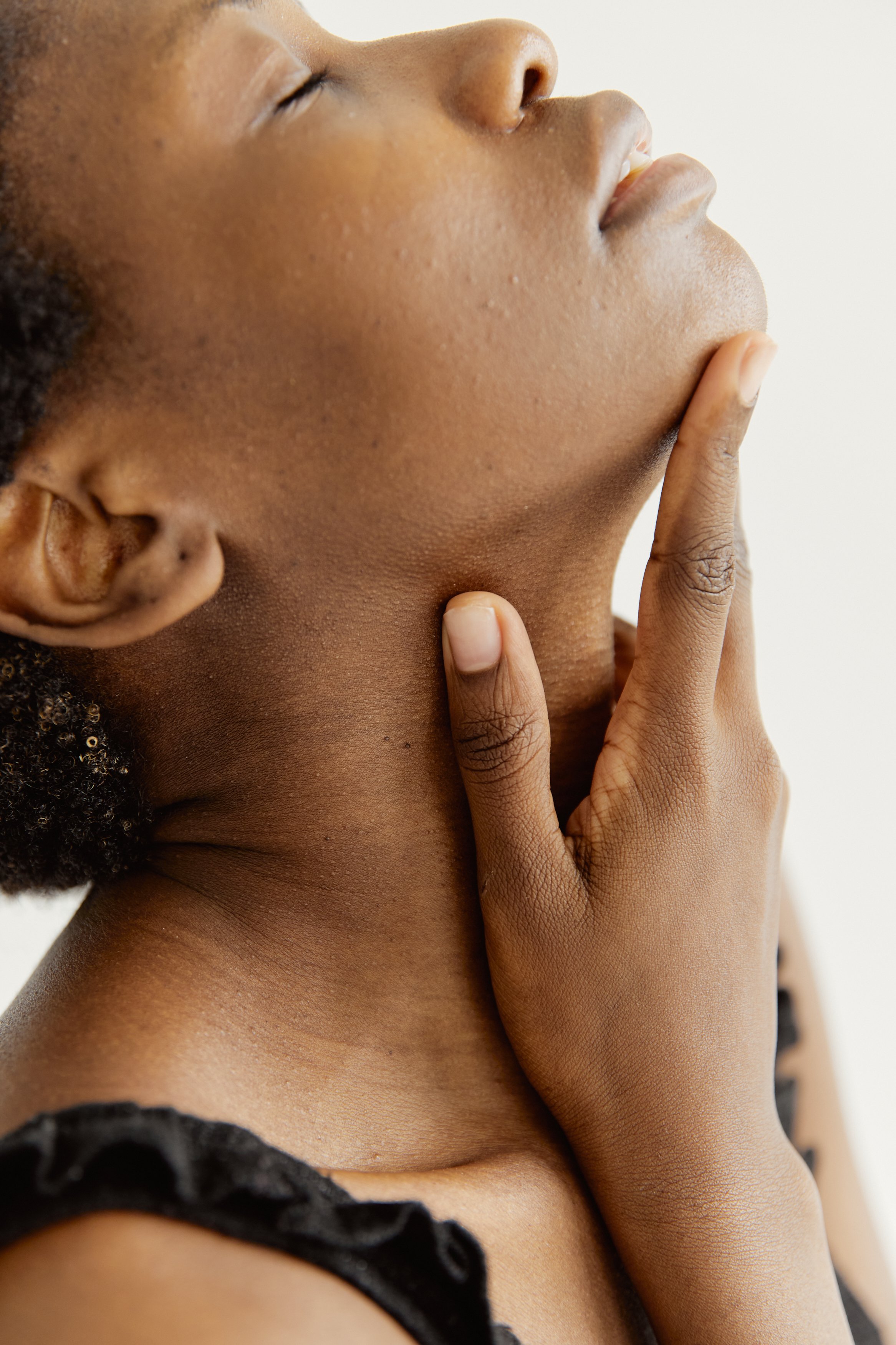 Close-up side view of a woman gently touching her neck with eyes closed, showcasing calmness and elegance.