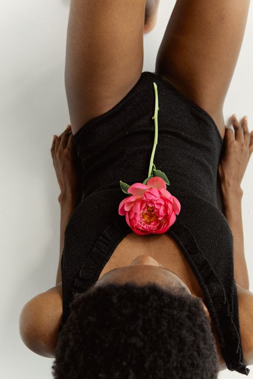 Free Artistic overhead shot of an adult woman in a swimsuit lying down with a pink flower. Stock Photo