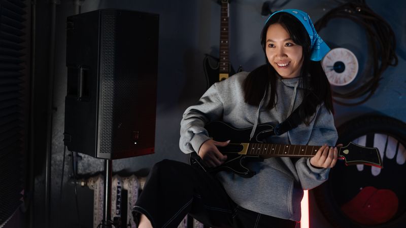 An enthusiastic young woman playing a video game with a guitar controller indoors, showcasing gaming joy.
