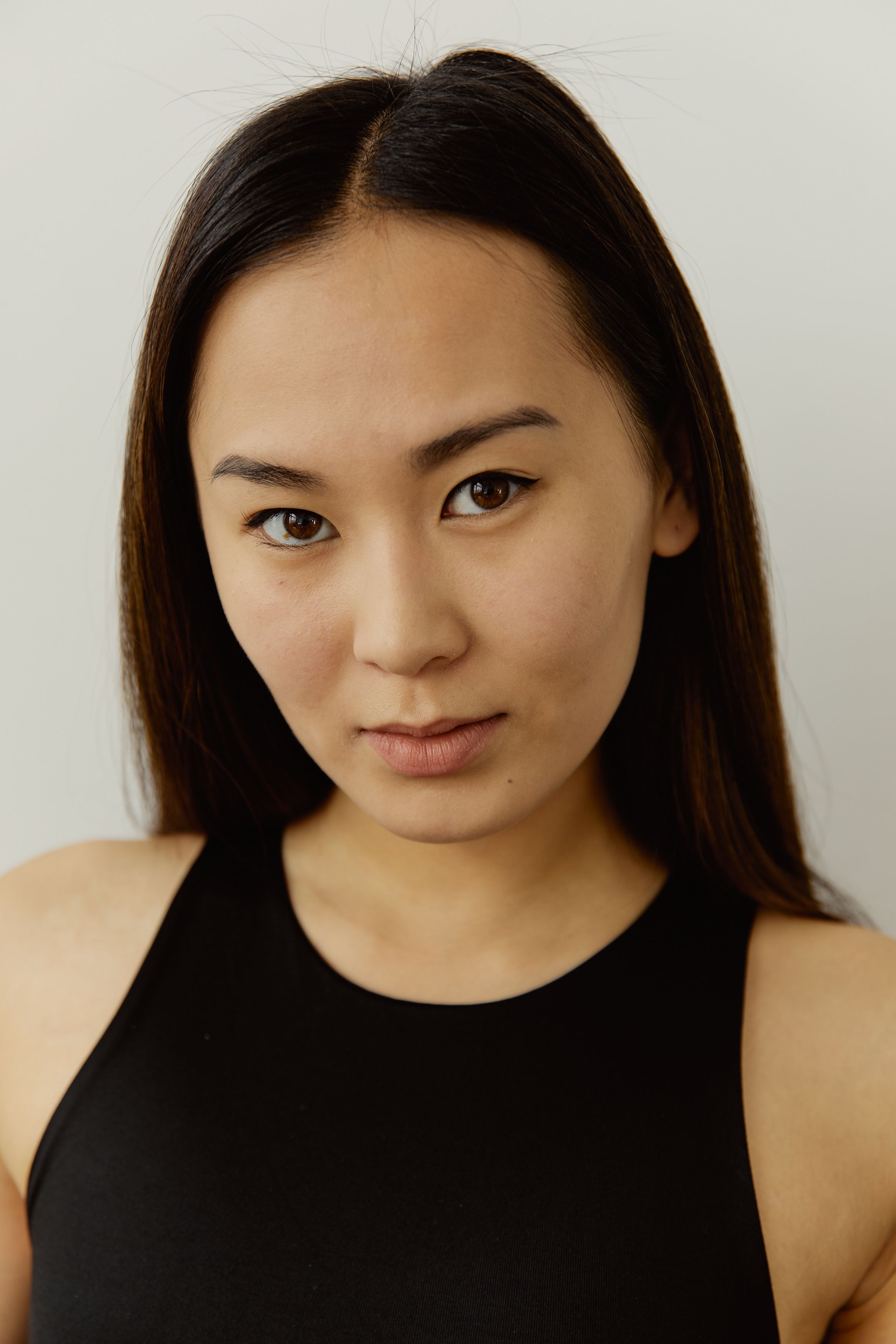Close-up portrait of a woman in a black tank top with a neutral expression against a plain background.