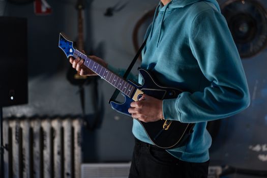 A person wearing a blue hoodie playing a guitar in a dimly lit room.
