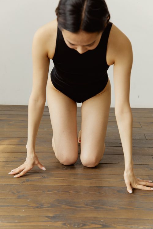 Free A woman in a black outfit kneels on a wooden floor in a yoga pose, focusing on mindfulness and balance. Stock Photo