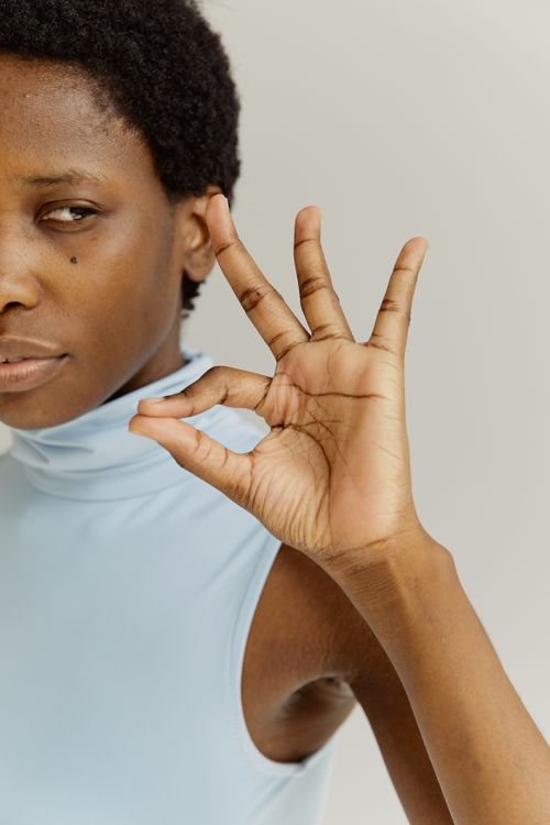 Free A modern portrait showcasing a woman making an OK hand sign against a plain background. Stock Photo