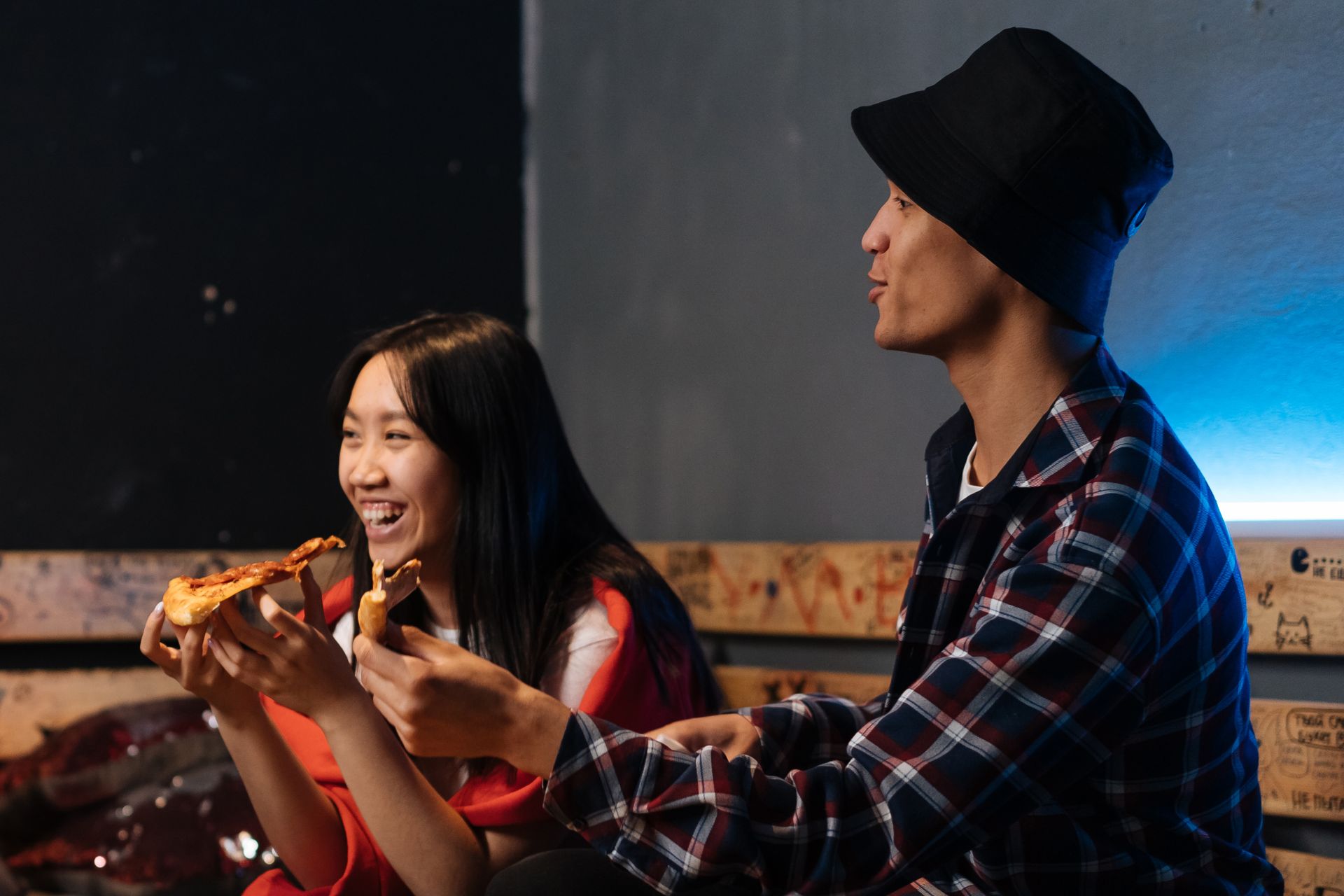 Two friends laughing and enjoying pizza together in a cozy indoor setting.