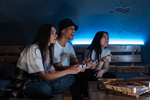 Group of friends laughing and playing video games indoors, enjoying pizza and fun together.