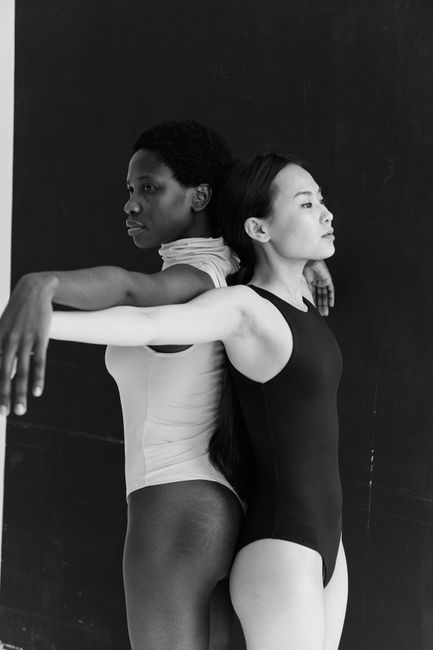 Black and white photo of two diverse women in a graceful dance pose, emphasizing contrast and harmony.