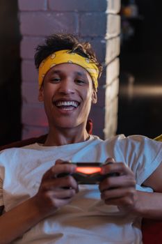 A young man with a bright smile and bandana enjoys video gaming indoors, creating a lively and fun atmosphere.