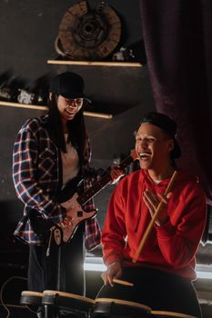 Two young adults enjoying a jam session with guitar and electronic drums.