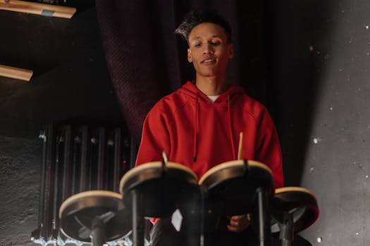 A young adult playing drums indoors, showcasing musical artistry. Dark ambient lighting adds depth.