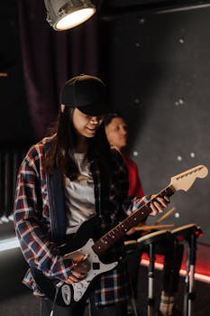 A musician in casual wear playing an electric guitar under stage lights, smiling.