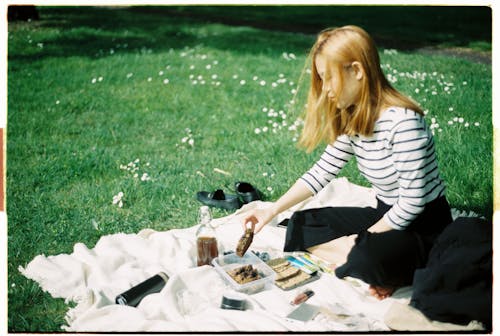 Woman in White and Black Striped Shirt Having A Picnic On Grass Field