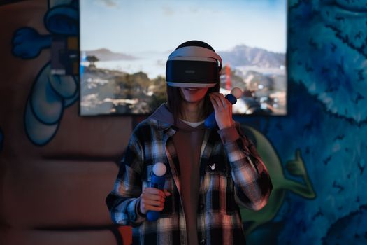 A young woman immersed in a virtual reality experience using VR goggles and controllers indoors.