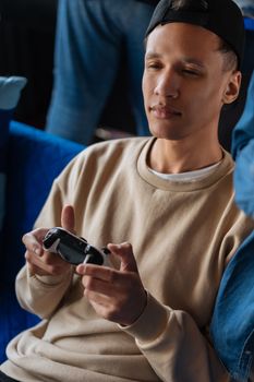 Young man playing video games indoors with a controller, wearing a sweater and cap.