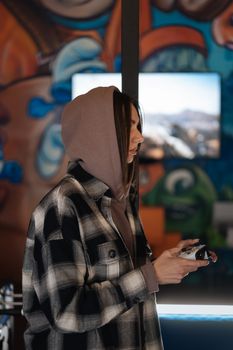 Side view of a young woman in a hoodie playing video games indoors with a joystick.