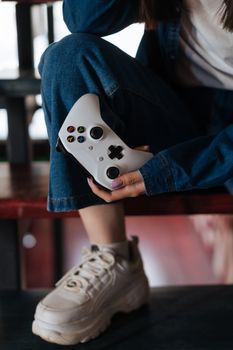 Person holding an Xbox controller while sitting on stairs, dressed in casual denim and sneakers.