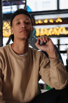 A stylish young man in a beige sweater holding a game controller indoors.